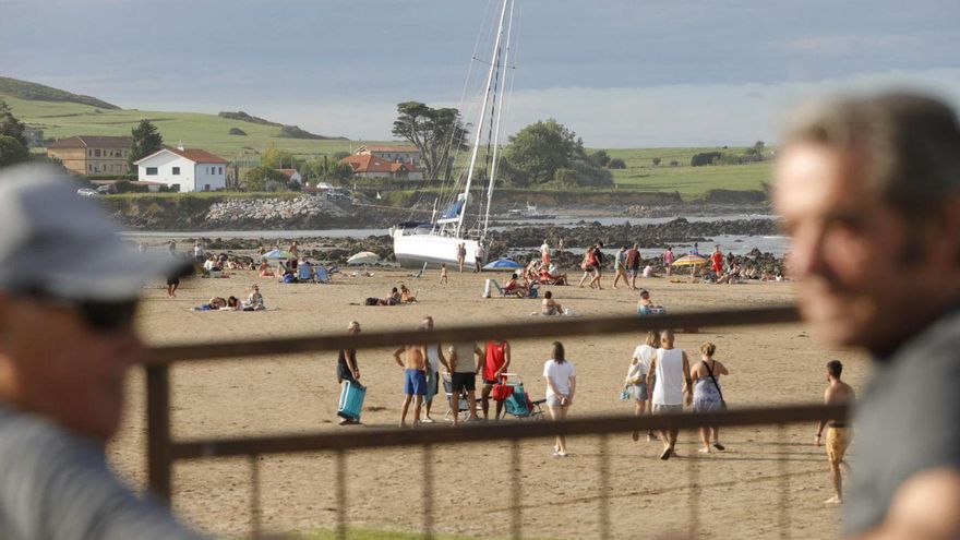 Dos vecinos, sentados frente al velero varado en la playa de Bañugues. | Ricardo Solís