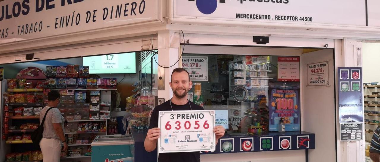 Óscar Sánchez, con el cartel del tercer premio, delante de su administración de loterías del Mercacentro, en Vecindario . | | LP/DLP