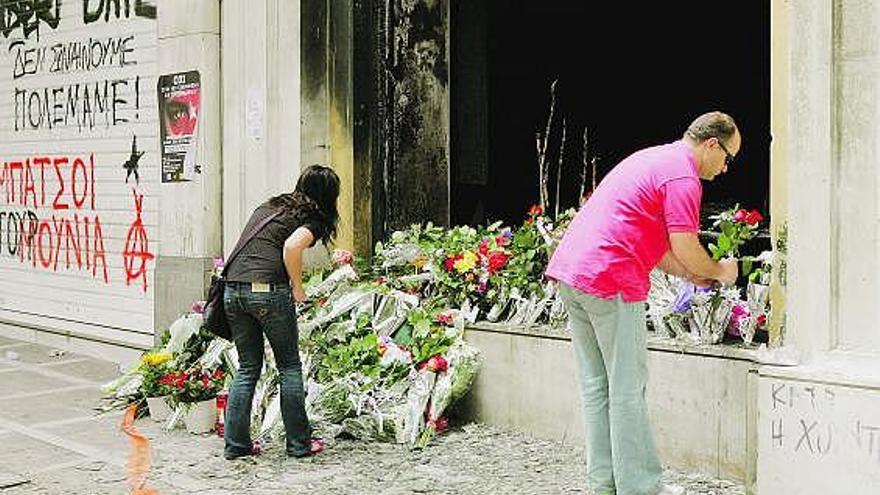 Duelo en atenas. Varios ciudadanos griegos depositan flores ante un banco, ayer, para rendir homenaje a las tres personas fallecidas el pasado miércoles en el incendio de la entidad, provocado por varios manifestantes.