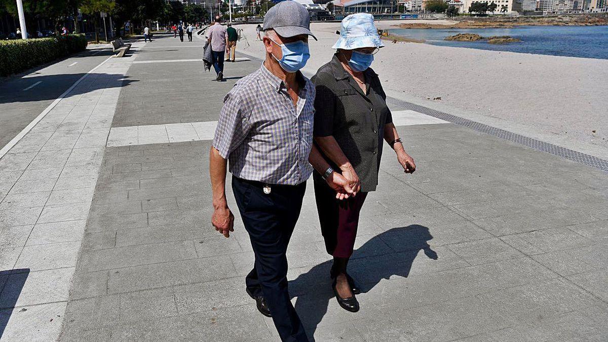 Una pareja con mascarilla camina por el paseo marítimo de A Coruña.