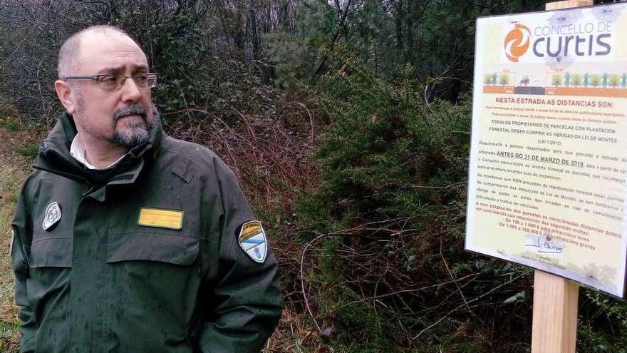 Ramón Fernández junto a uno de los carteles que han instalado en Curtis para instar a cumplir las distancias.