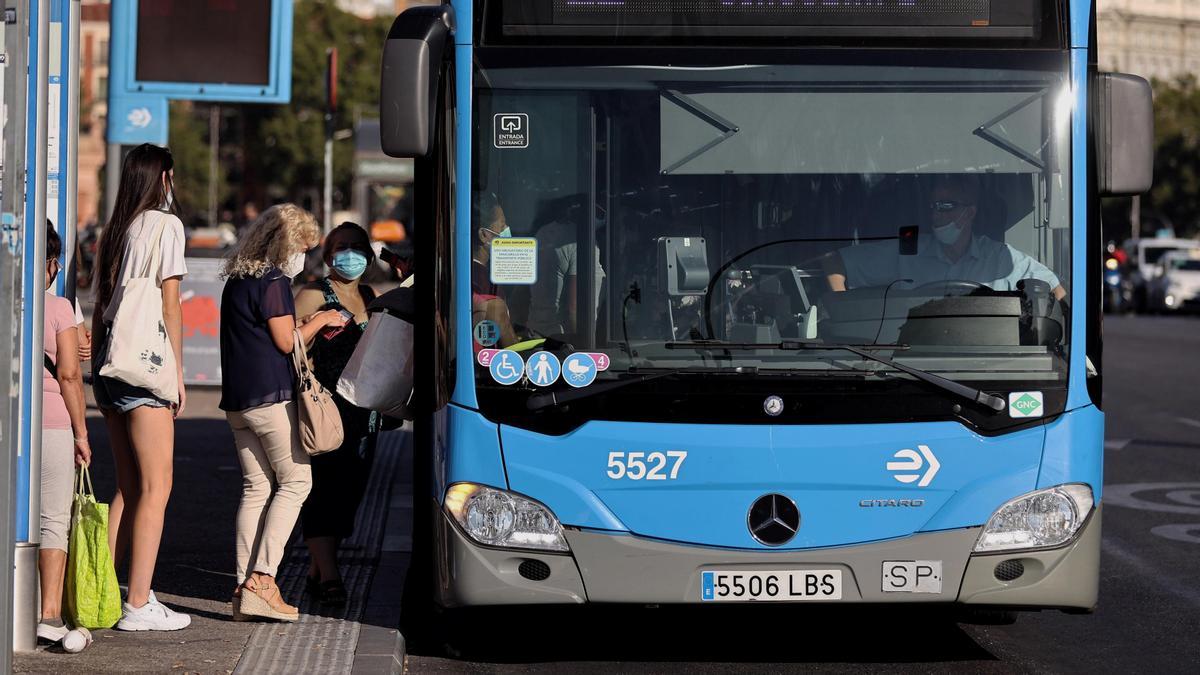 Varias personas hacen cola en Madrid para subir a un autobús.