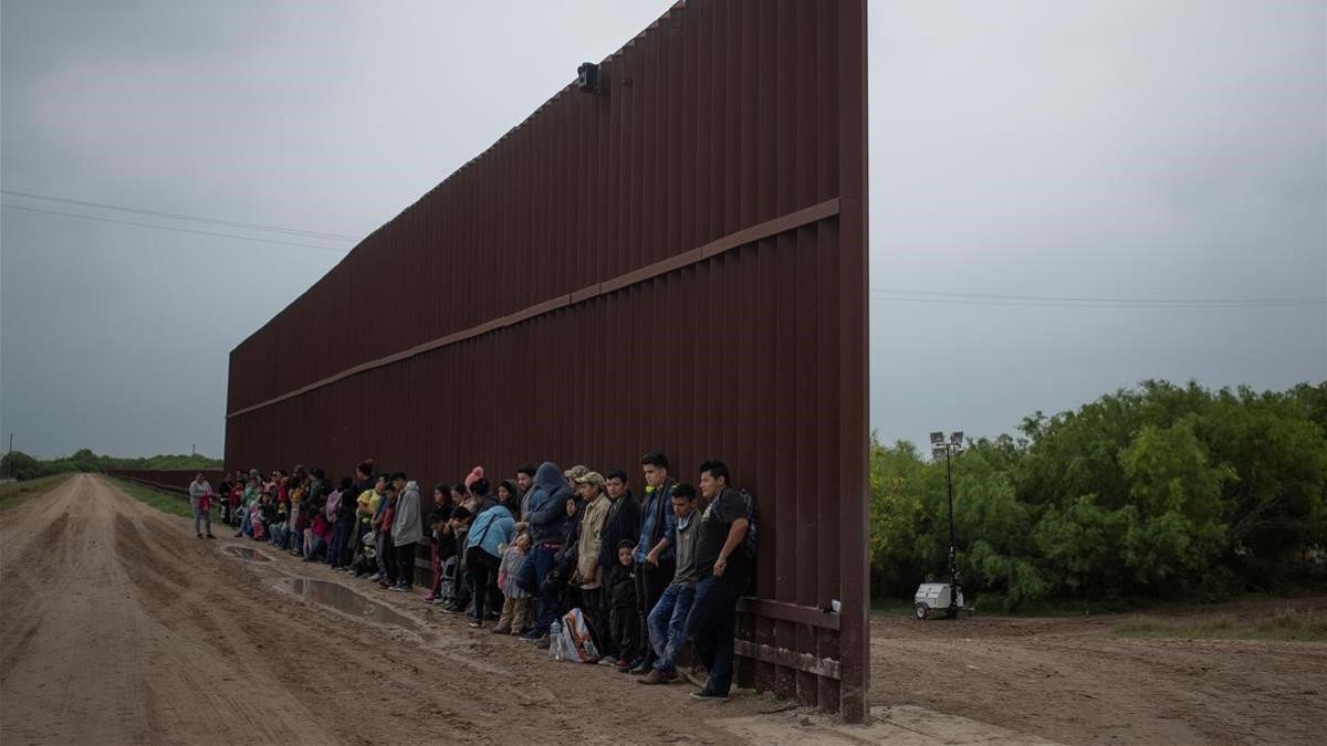 Migrantes centroamericanos aguardan en el lado mexicano del muro a cruzar al lado estadounidense.