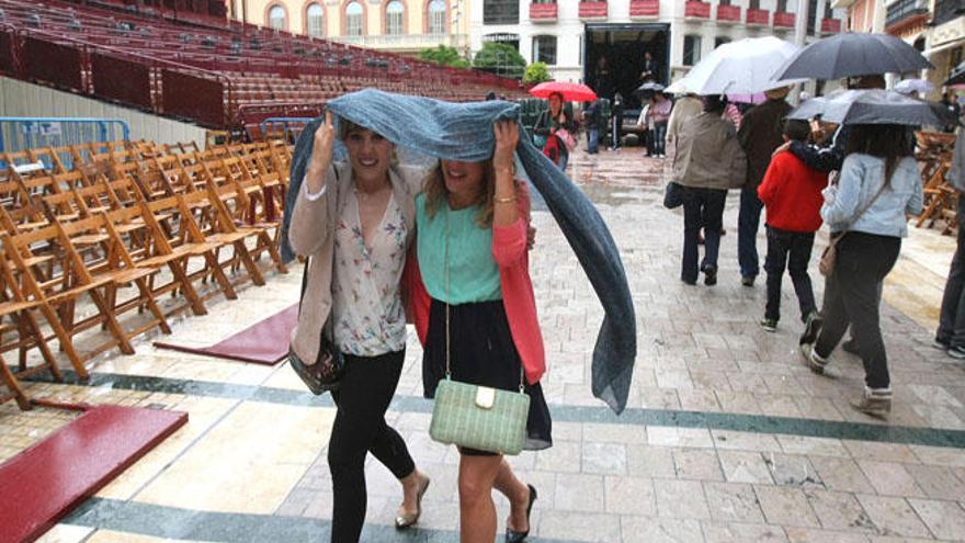 Viandantes por la calle Larios intentando resguardarse de la lluvia.