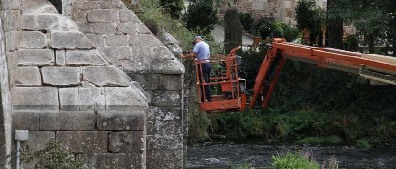 Un operario retira la maleza acumulada en uno de los arcos del puente. // Bernabé