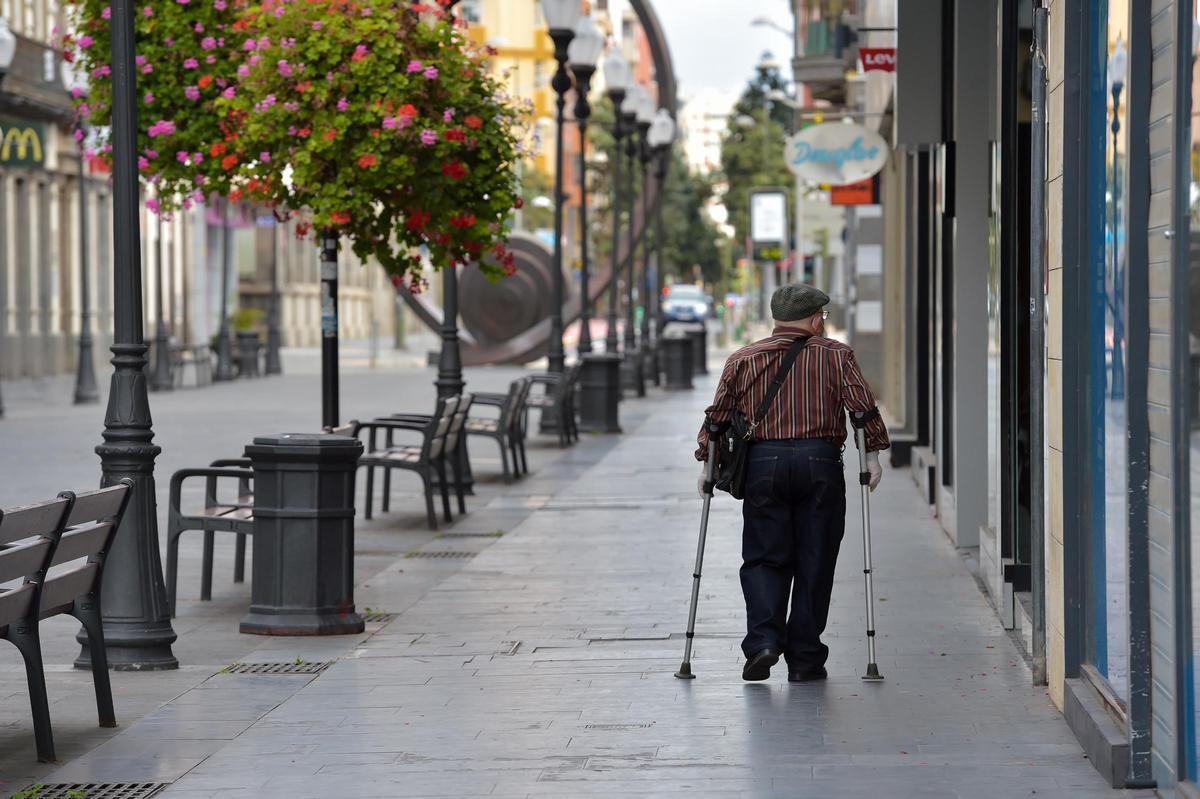 Un señor mayor pasea por Triana con muletas.