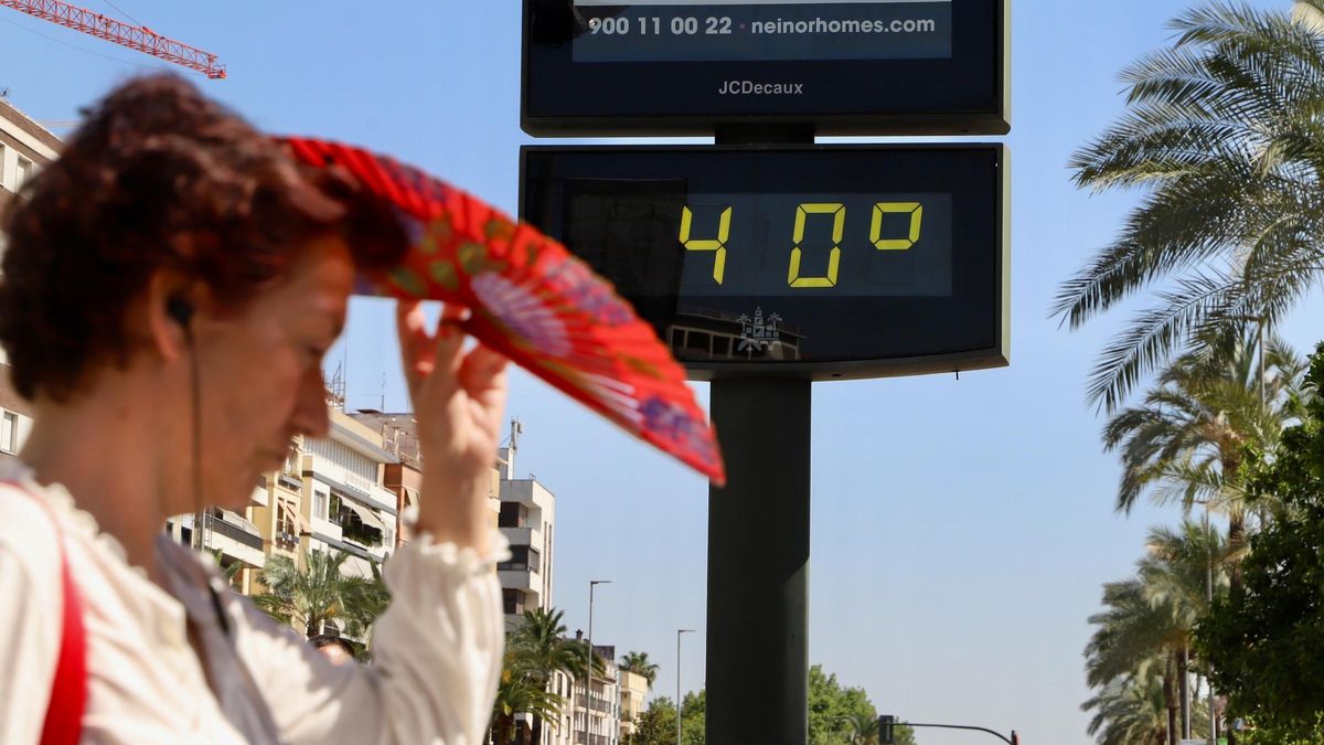 Una mujer se refugia del sol bajo su abanico mientras camina ante un reloj, en Córdoba capital.