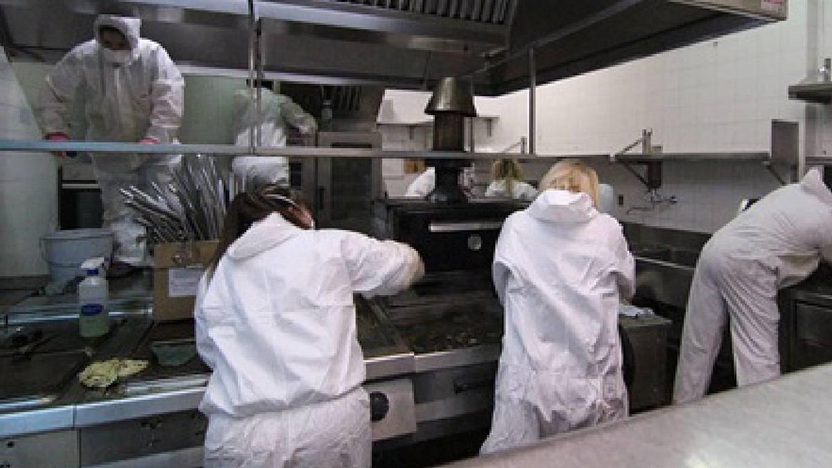 Varios empleados limpian una cocina de restaurante con equipos de protección.