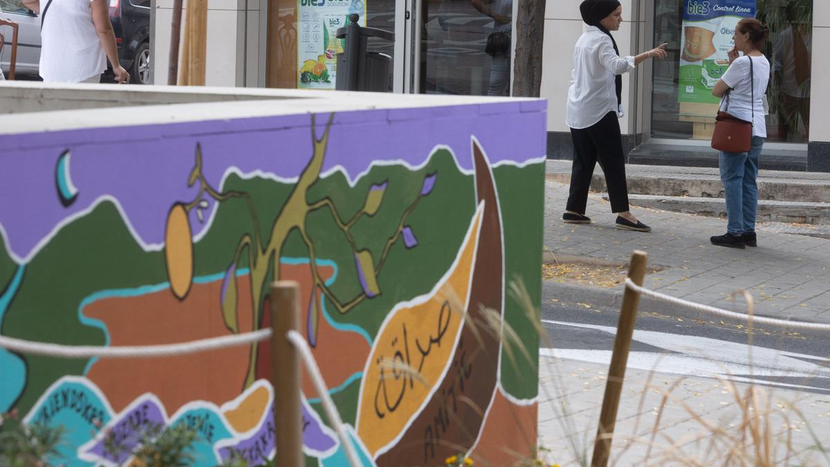 Personas de diferentes orígenes charlan junto a un mural pintado por María Balibrea.