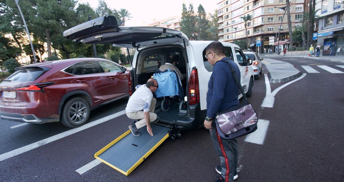 El conductor de uno de los eurotaxis que operan en el municipio  ayuda a subir a un usuario, en la plaza Circular.  | JUAN CARLOS CAVAL