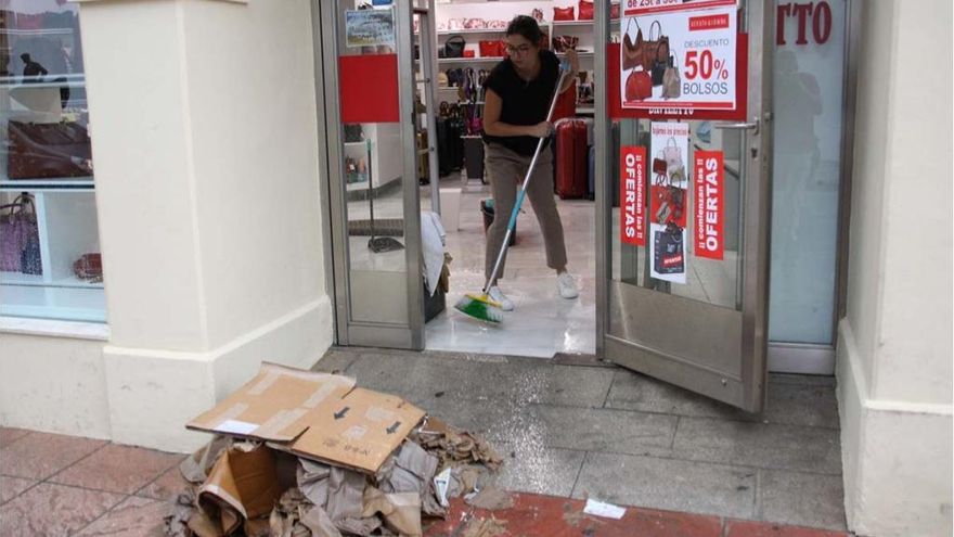 Una joven se esfuerza en sacar el agua de un local comercial.