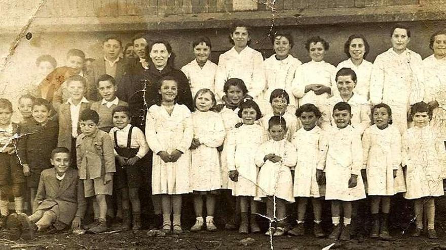 Doña Tinita posa con sus alumnas, vestidas de Hijas de María, frente a uno de los hórreos de Vilatuxe.