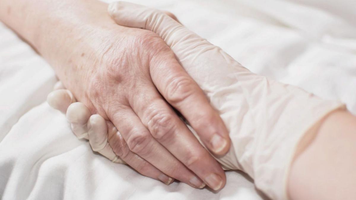 Una sanitaria da la mano a una hospitalizada en estado grave, en una imagen de archivo. | EL PERIÓDICO
