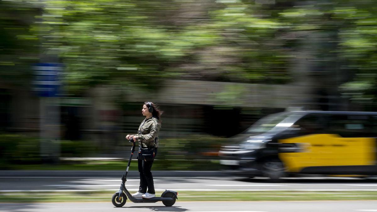 Un usuari de patinet elèctric circula amb auriculars pel carril bici del passeig de Sant Joan de Barcelona. | JORDI COTRINA