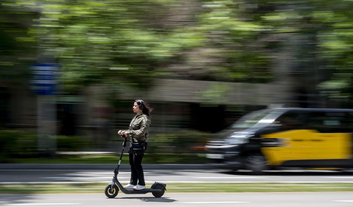 Un usuari de patinet elèctric circula amb auriculars pel carril bici del passeig de Sant Joan de Barcelona. | JORDI COTRINA