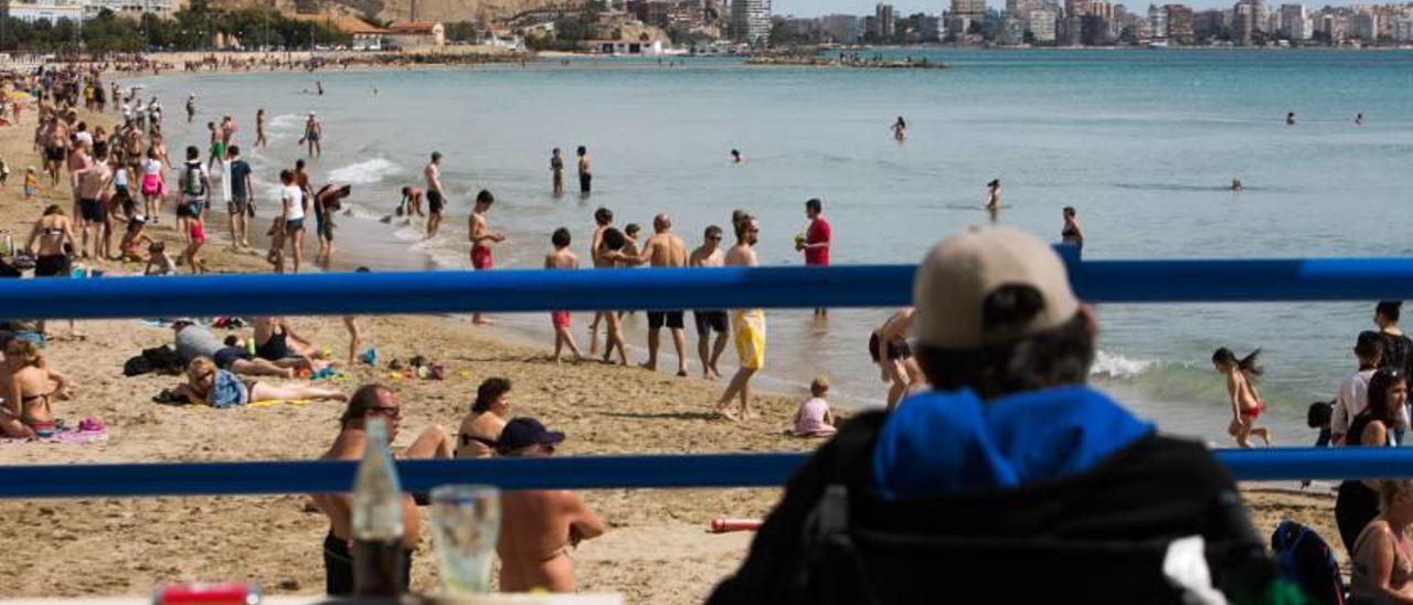 Un persona observa a los bañistas en la playa alicantina del Postiguet mientras se toma un refresco durante el pasado puente de Pascua.