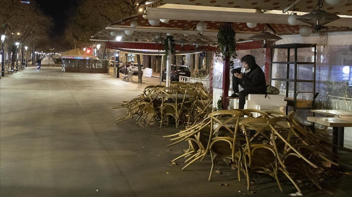 Un sintecho carga su móvil en la terraza de la Rambla de Catalunya en la que se cobija durante el toque de queda.