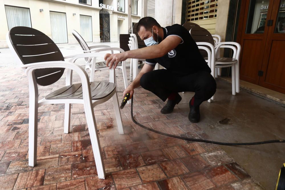 Imágenes de una lluviosa mañana de jueves en el centro de Málaga, donde al paisaje ya habitual de pocas personas y la mayoría de ellas con guantes y mascarillas se le han añadido los preparativos de bares, cafeterías y terrazas que se preparan para el inminente cambio de fase de la desescalada de la ciudad.