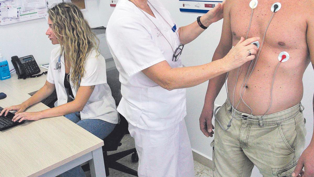 Una sanitaria pega los electrodos en el pecho a un paciente para realizarle un electrocardiograma en la consulta