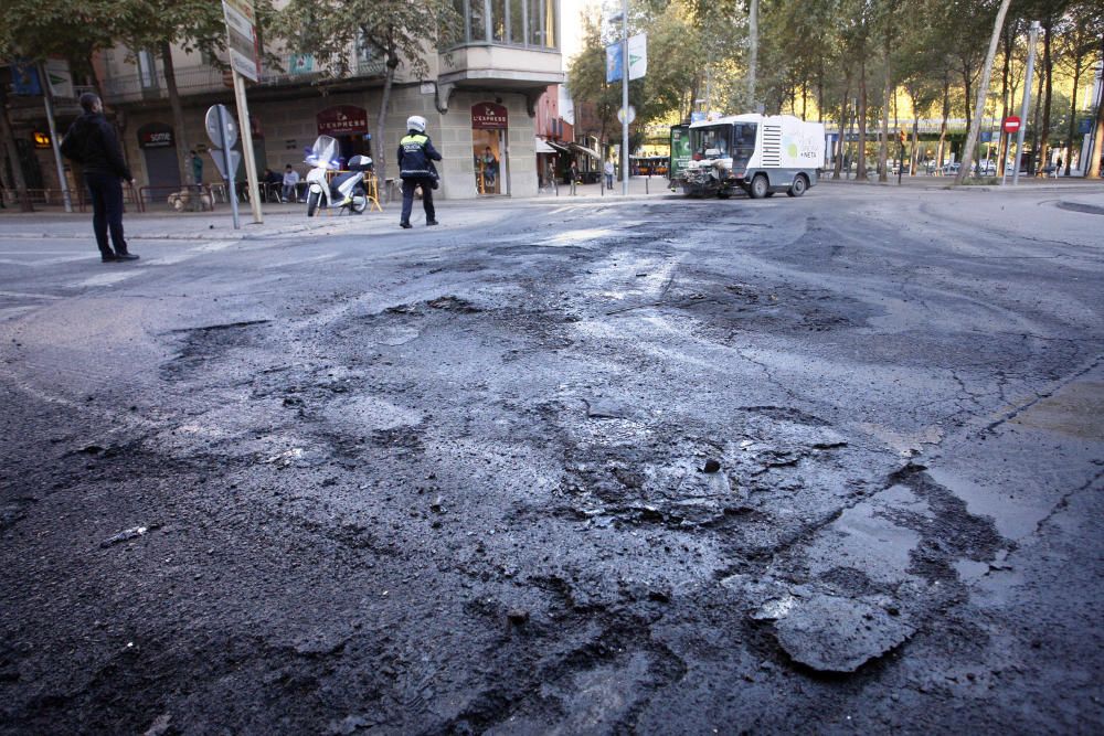 Carrers amb restes de mobiliari urbà cremat, contenidors per terra i treballadors de la brigada treballant