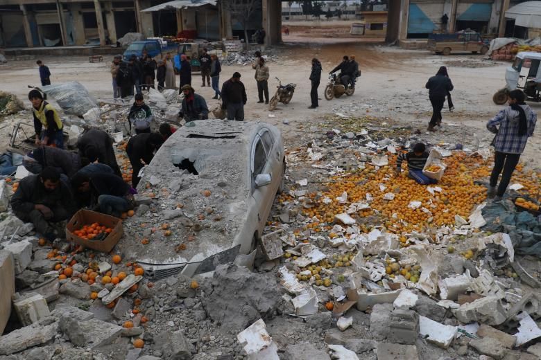 La gent recull taronges disperses enmig de de la runa després d'un atac aeri en un mercat rebel celebrat a la ciutat de Maarrat Misrin a la província d'Idlib, a Síria, el 14 de gener.