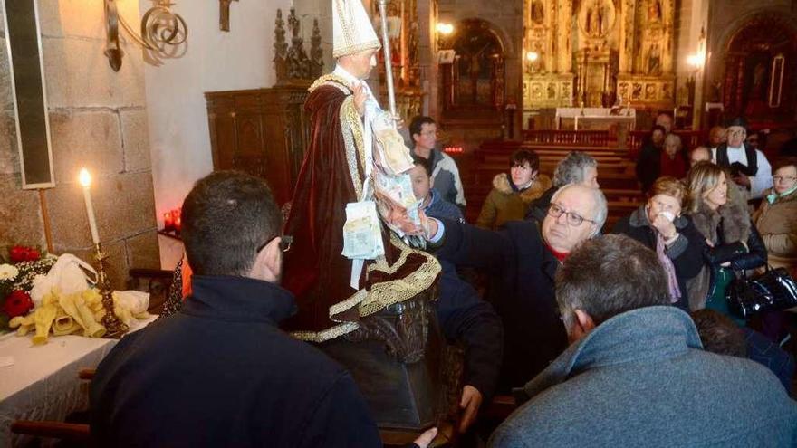 Los fieles pasan la estampita por el manto del santo, que procesionó adornado con billetes. // Rafa Vázquez