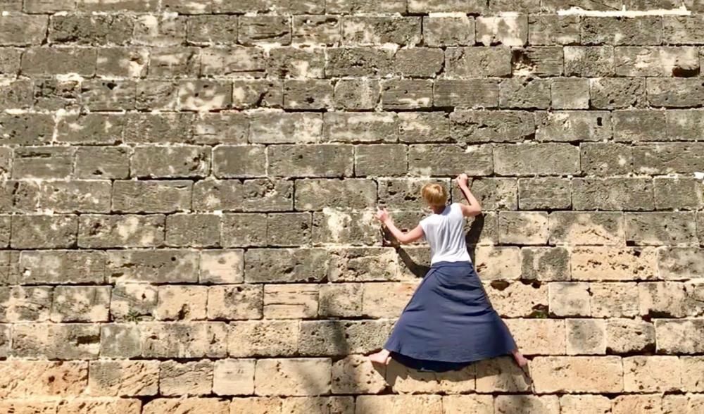 Una turista practica la escalada en las murallas de Palma descalza y con falda