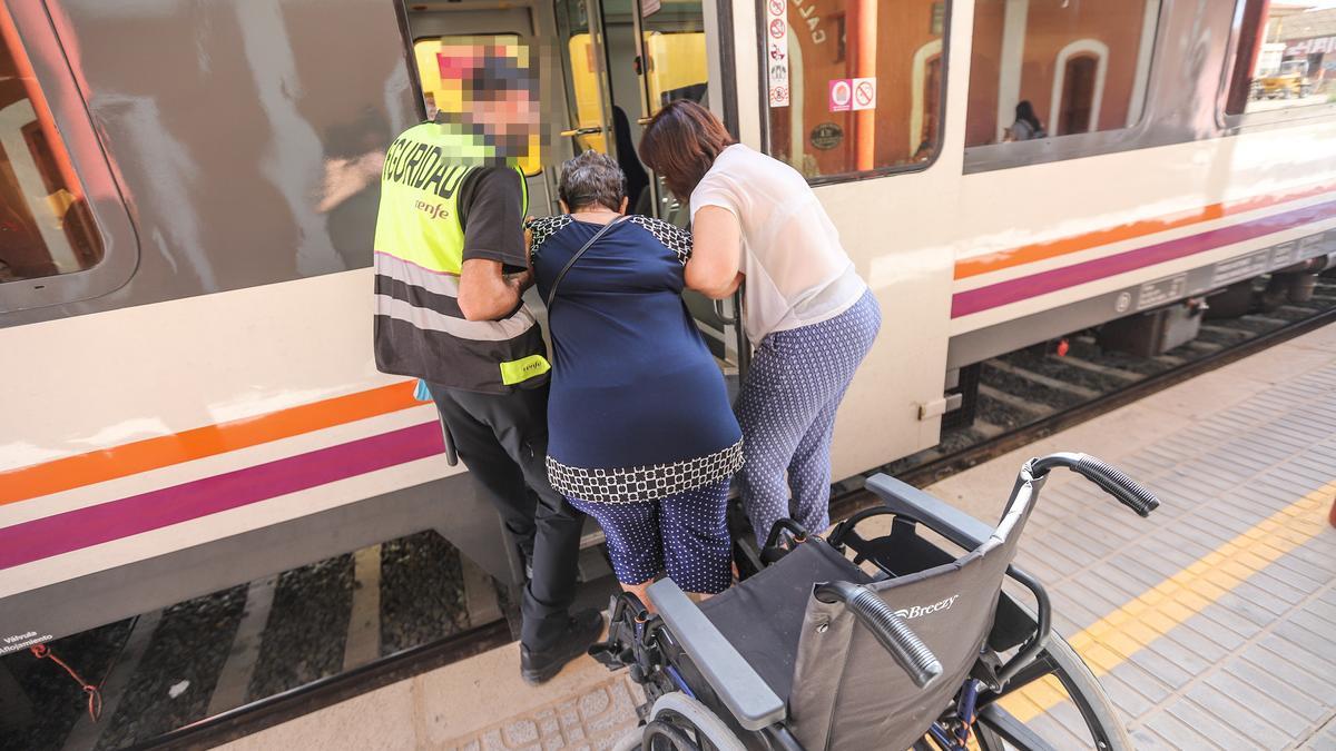 Una mujer y un trabajador ayudan a una persona en silla de ruedas a subir al cercanías Alicante-Murcia.