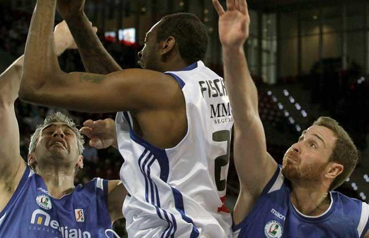 El pívot norteamericano del Real Madrid, D'or Fischer (c), busca el pase entre el ala-pívot del Alicante, Guillermo Rejón (i) y su compañero, y el escolta Álex Urtasun (d), durante el partido, correspondiente a la vigésimo quinta jornada de Liga ACB, que ambos equipos disputan esta mañana en la Caja Mágica de Madrid.