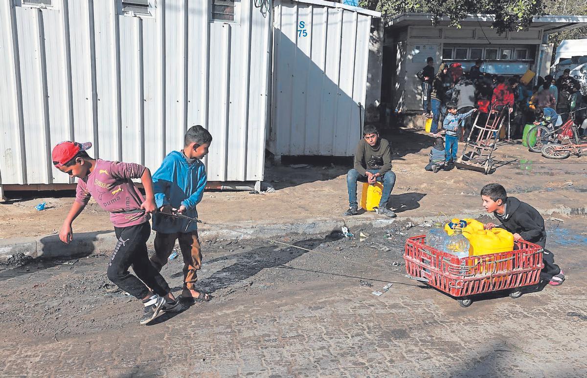Unos niños del barrio de Al-Shaboura arrastran unas garrafas de agua hasta sus tiendas de campaña, en la ciudad de Rafah.