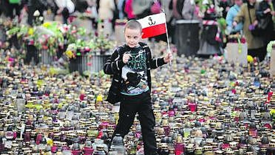 Un niño con una bandera polaca pasa entre miles de velas.