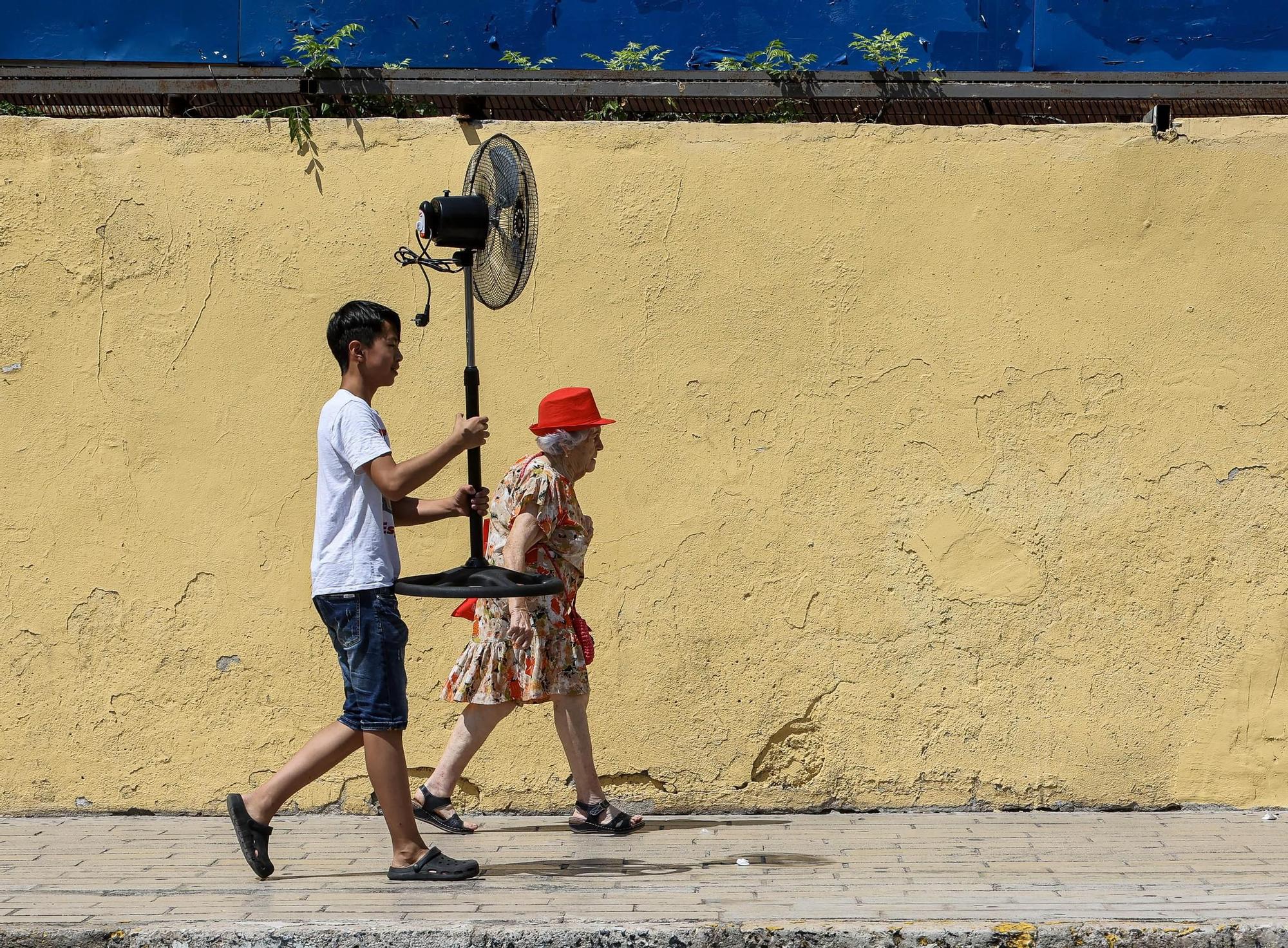 El empleado de un comercio asiático carga con el ventilador recién comprado por una clienta durante una ola de calor en Alicante.  26.06.23
