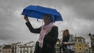 Archivo - Dos mujeres intentan protegerse del viento con su paragüas mientras caminan por el Puente de Isabel II, en Sevilla (Andalucía).