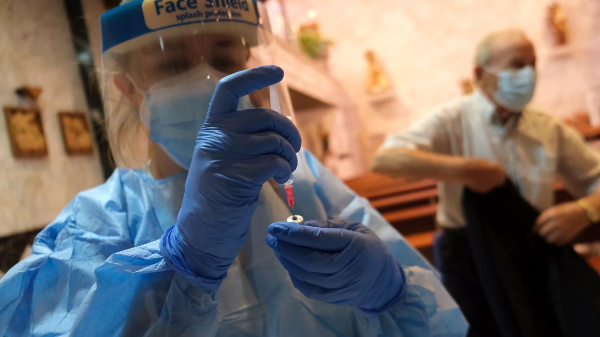 Una mujer sanitario prepara una vacuna vestida con un traje de protección frente al COVID.