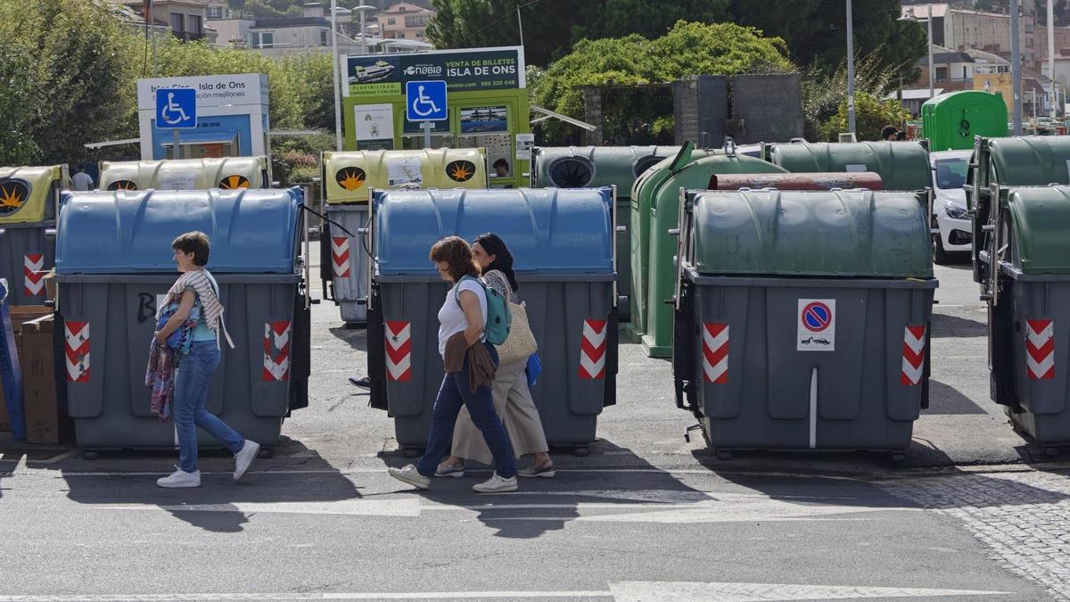 Varias personas pasan por delante de una isla de contenedores en la entrada al puerto de Bueu.