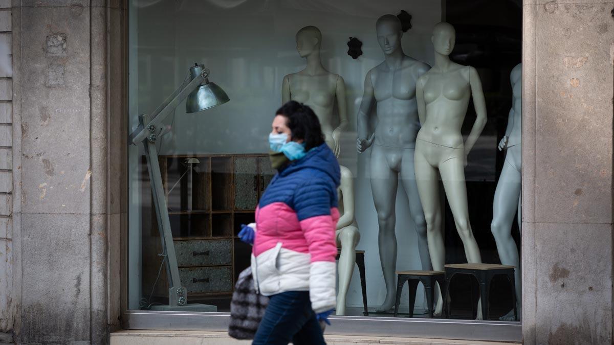 España roza los 80.000 casos de coronavirus. En la foto, una mujer con mascarilla y guantes pasa ante una tienda cerrada, en Barcelona.