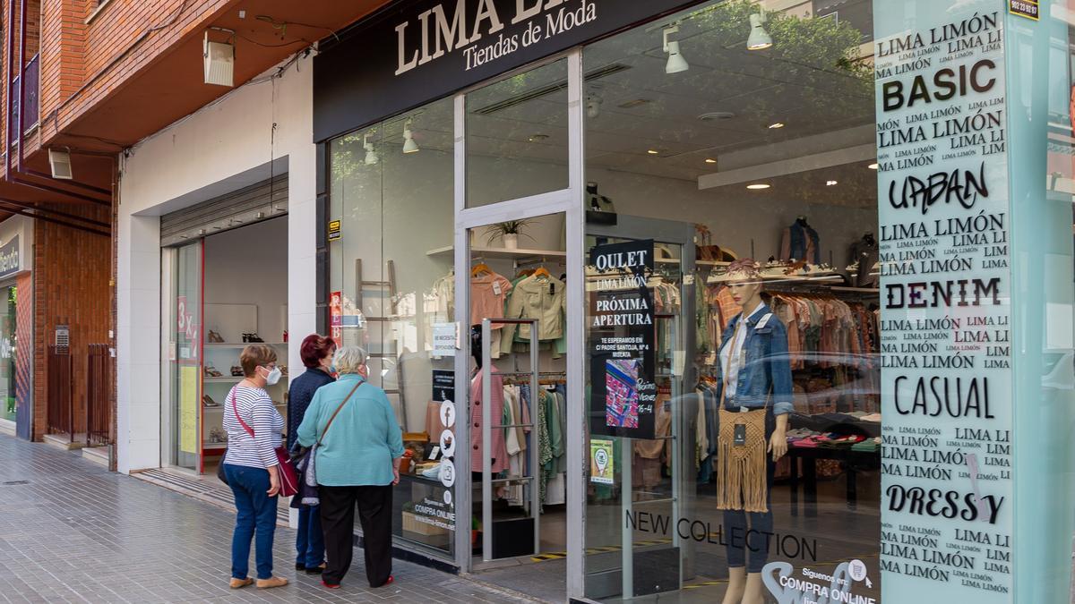 Mujeres ven el escaparate de una tienda de moda en Mislata.