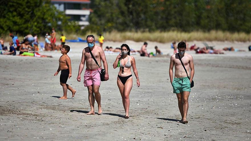 Varias personas con mascarilla en una playa gallega el pasado verano.