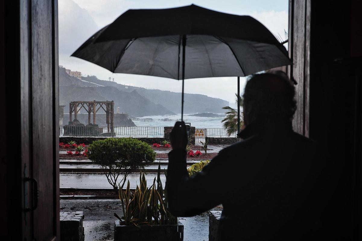 Un hombre se refugia bajo su paraguas mientras espera a que escampe.