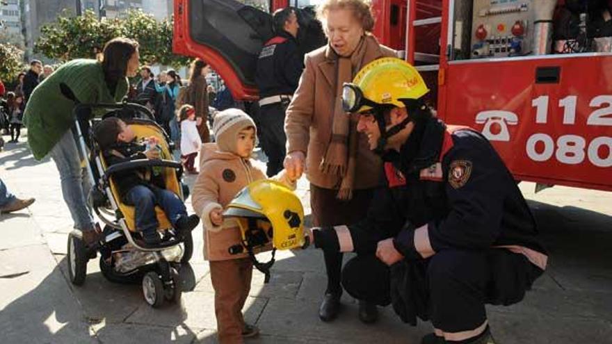 Un agente de bomberos muestra un casco a un niño al que acompaña su abuela durante la exposición en A Ferrería.  // Gustavo Santos