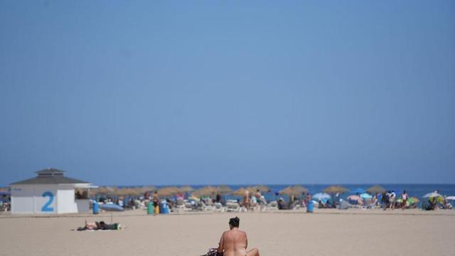 Una persona asseguda en una tovallola a la platja durant la quarta onada de calor de l’estiu, el 22 d’agost del 2023, a València, País Valencià (Espanya).