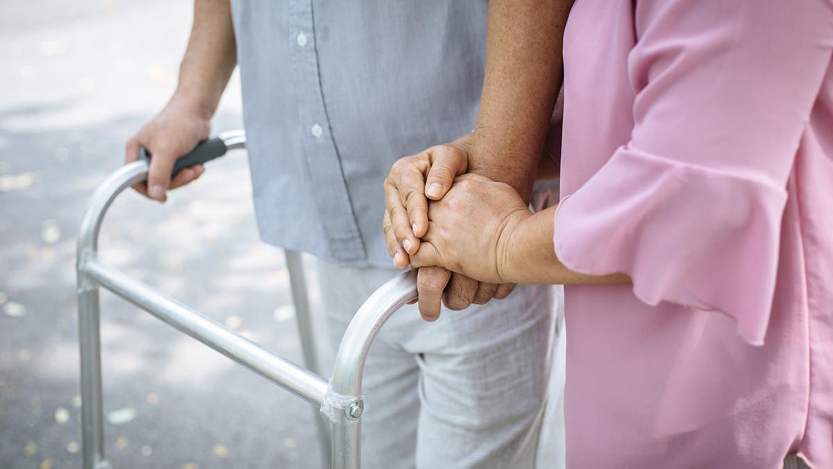 Una mujer ayuda a caminar a un hombre que utiliza un andador.