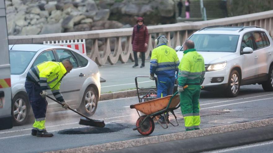 Operarios tapan baches, ayer, en el paseo marítimo.   | // IAGO LÓPEZ