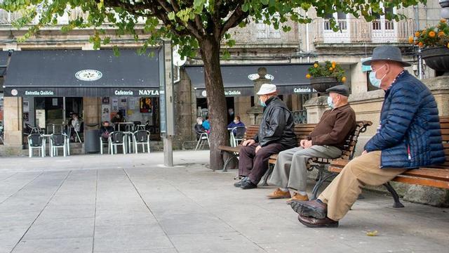Tres personas mayores observan una cafetería abierta en un Carballiño confinado.
