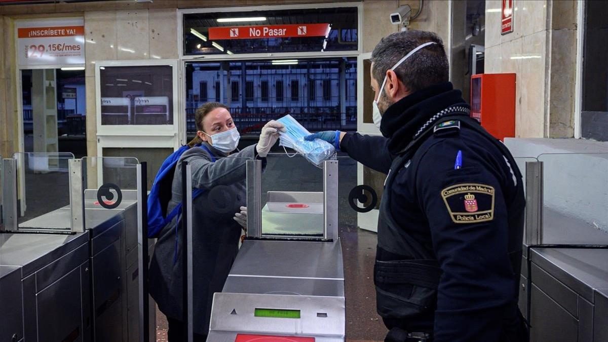 Un policía reparte mascarillas en la estación de tren de Alcalá de Henares, el 13 de abril del 2020