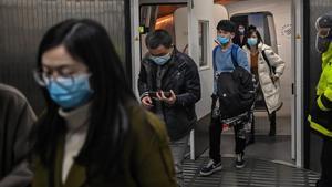 Pasajeros con mascarilla salen de un avión, tras aterrizar en el aeropuerto de Wuhan.