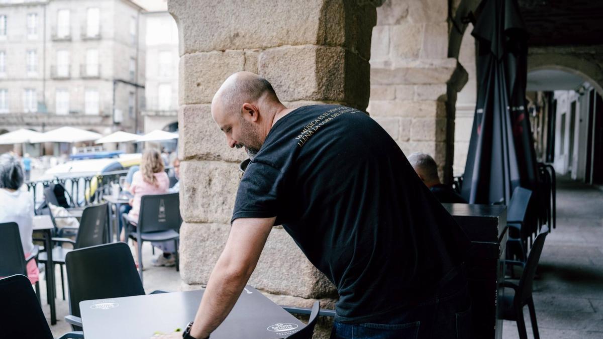 Un camarero limpia una mesa en el centro histórico de Ourense con el cielo encapotado.