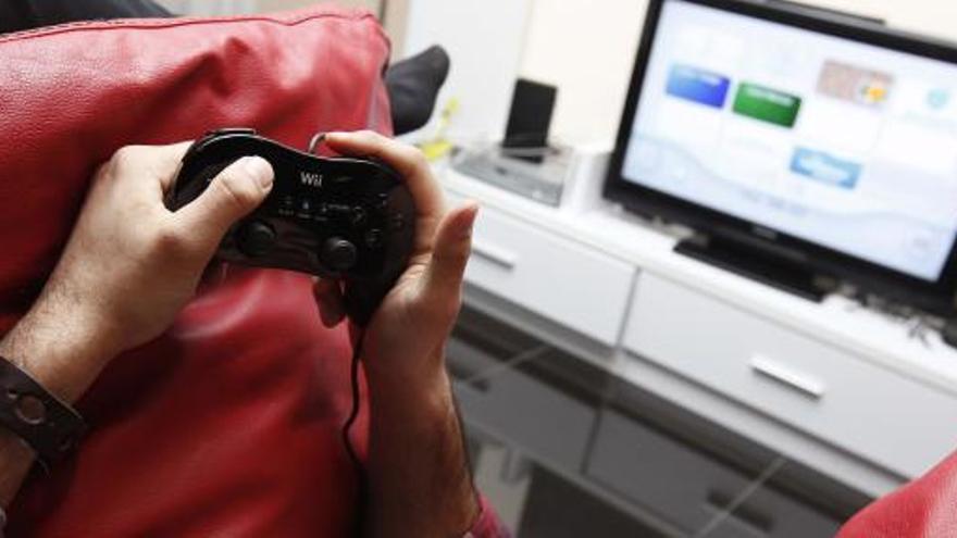 Un joven juega con su videoconsola ante la pantalla del ordenador desde el salón de su casa