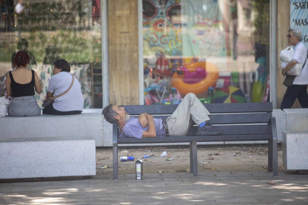 Un hombre duerme en uno de los nuevos bancos de la plaza.