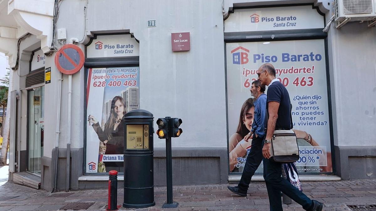 Dos hombres pasan ante dos grandes anuncios de ‘pisos baratos’ en una calle de Santa Cruz de Tenerife.